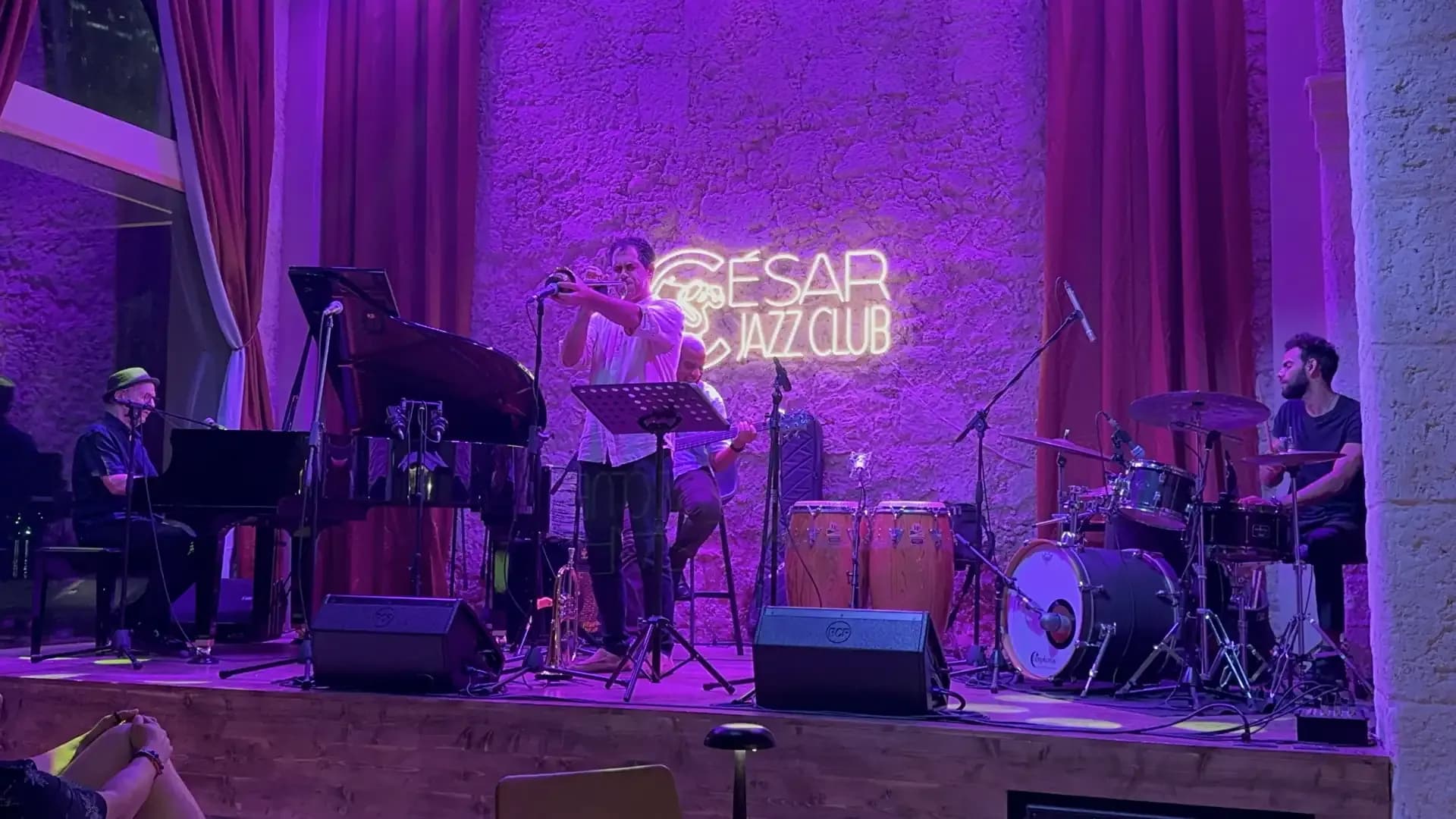 A jazz band performs on a stage under purple lights at Cesar Jazz Club.