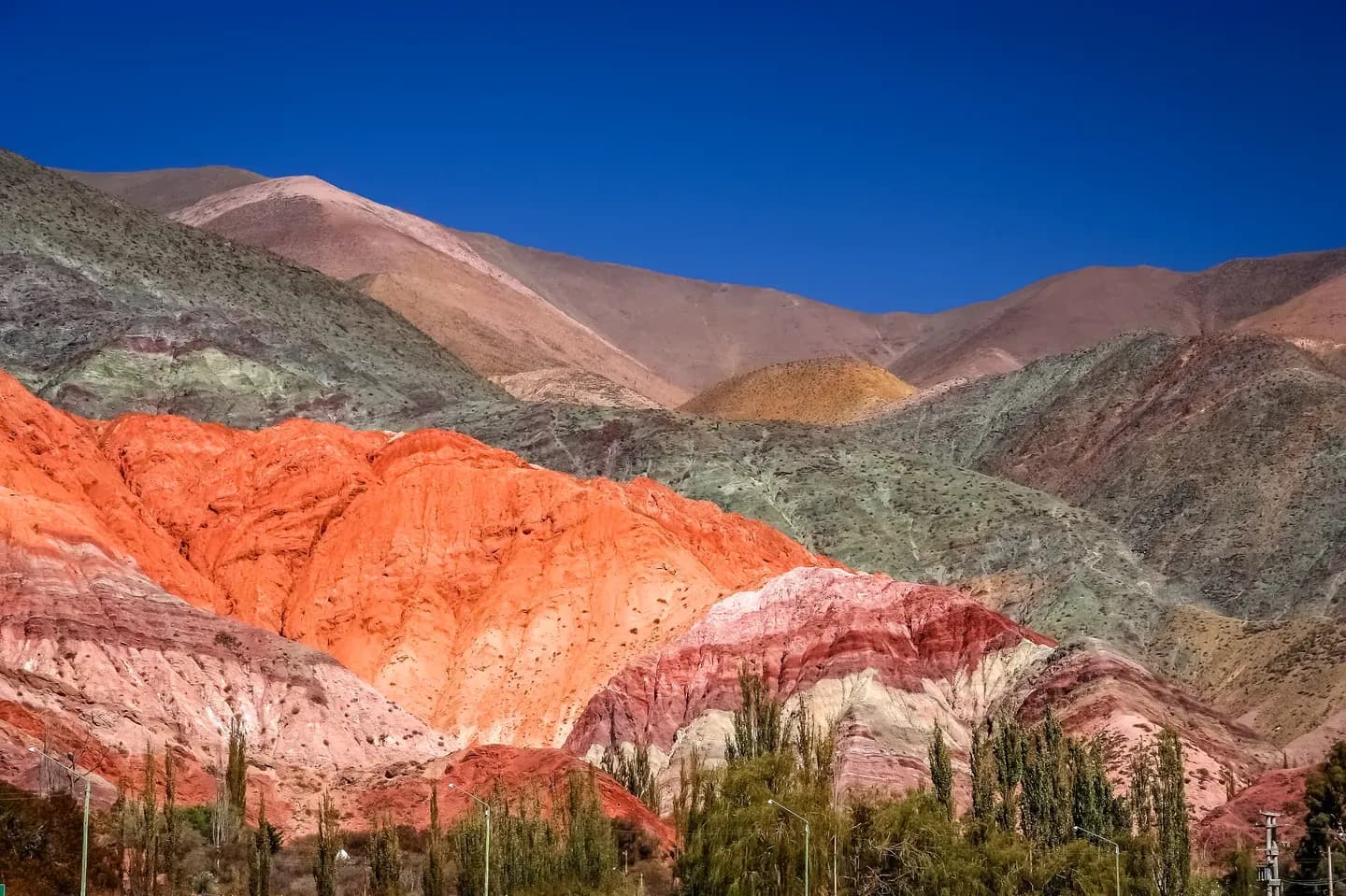 Orange, pink and grey striped hills above a line of poplar trees in the Quebrada de Humahuaca, Jujuy, Argentina