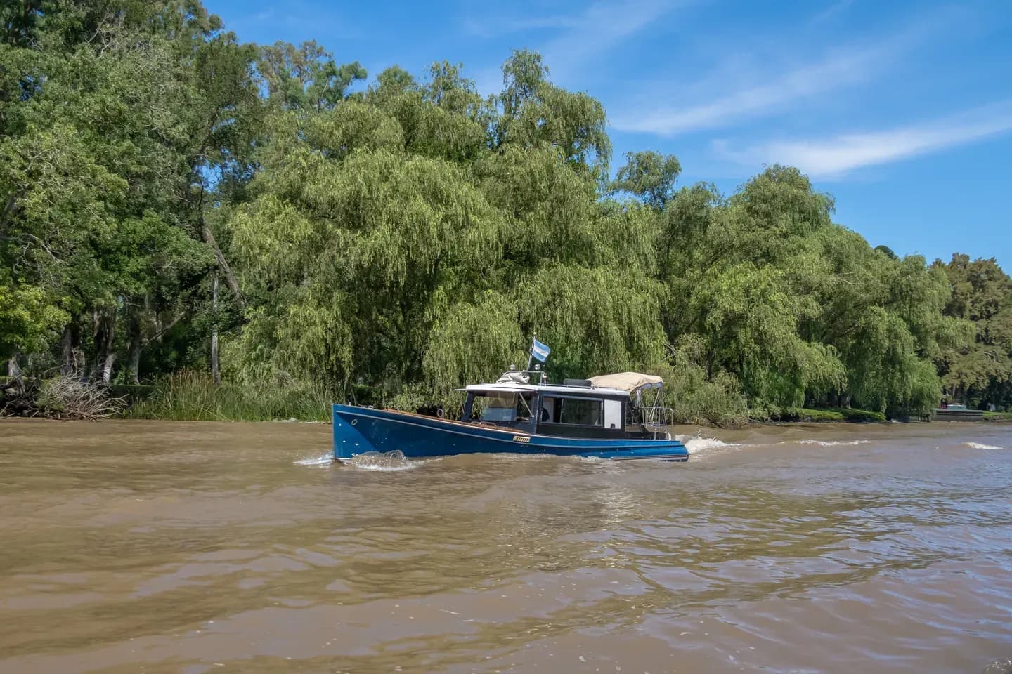 A blue launch on the brown water of the Tigre delta under willow trees, Buenos Aires province, Argentina