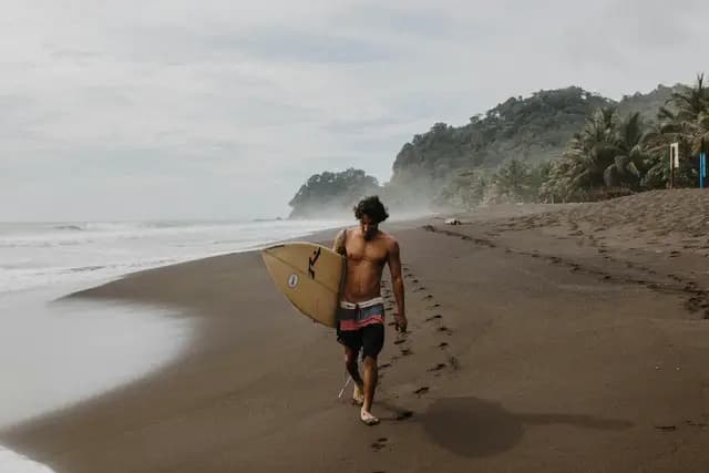 Surfer walking along a dark-sand Pacific beach in Costa Rica