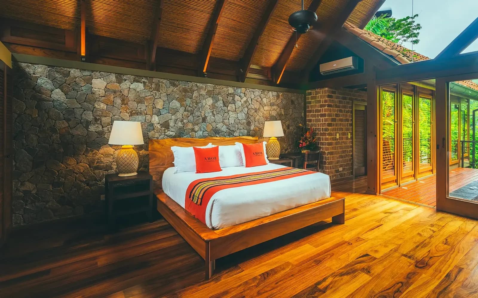 King bed in a Canyon Casita at Amor Arenal, stone wall and glass doors open to the forest