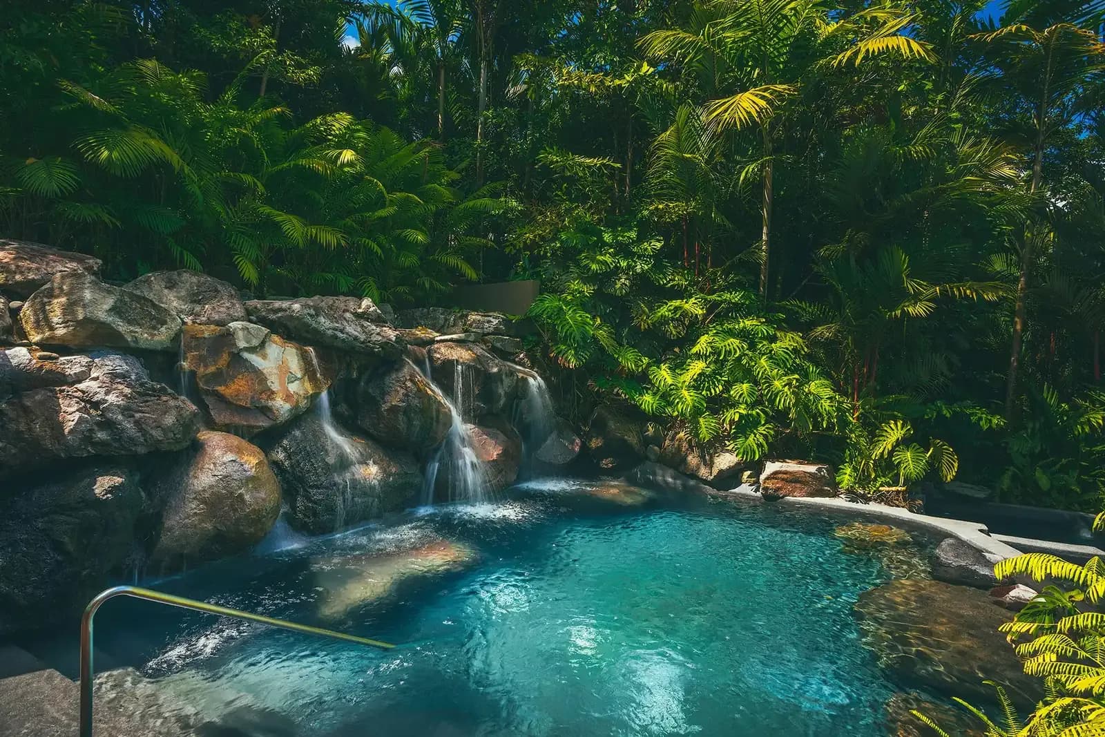 The spring-fed pool and waterfall at Amor Arenal lit at night among palms