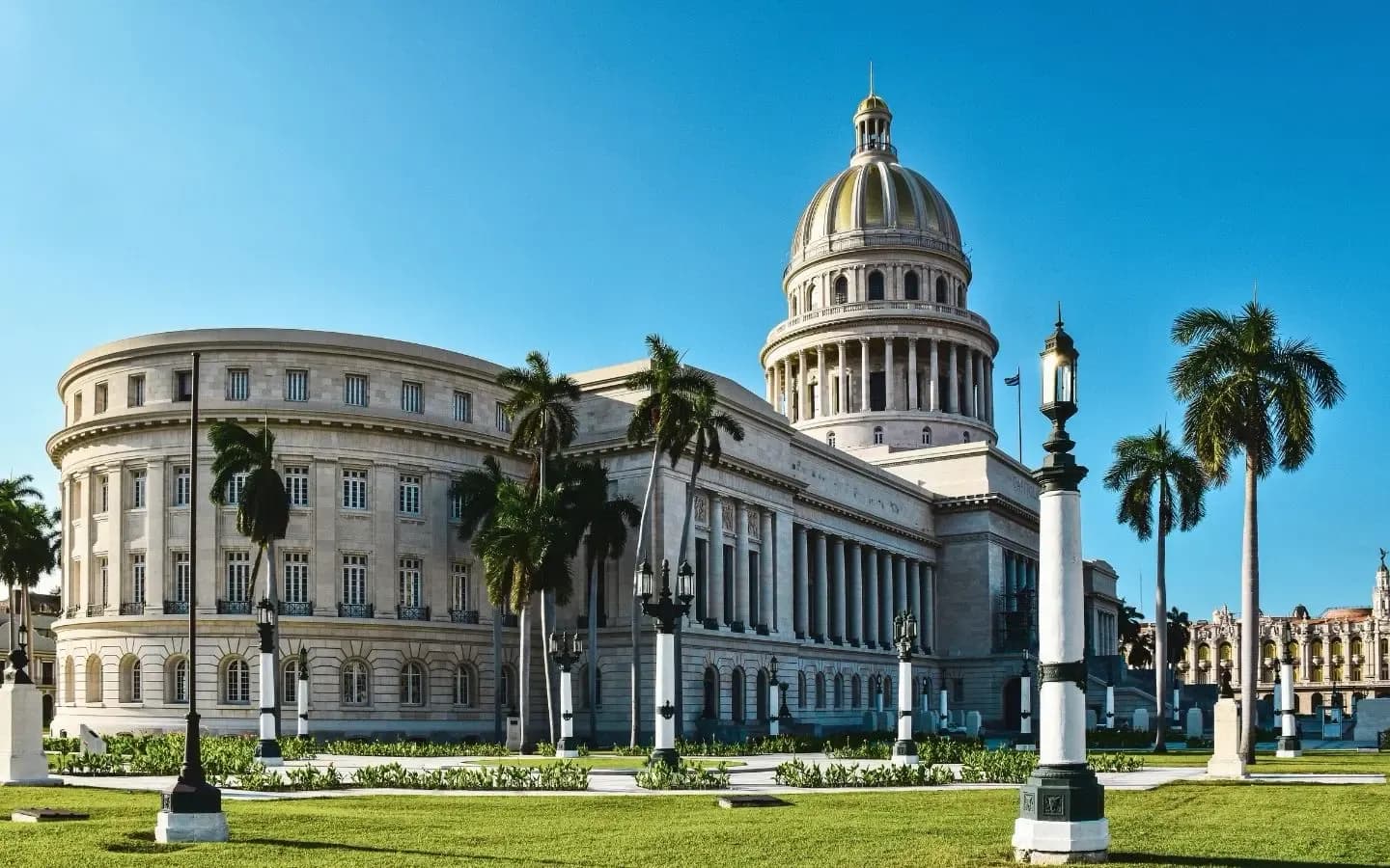 The neoclassical Capitolio Nacional in Havana, Cuba, stands under a clear blue sky, with its iconic dome, grand colonnade, and surrounding palm trees.