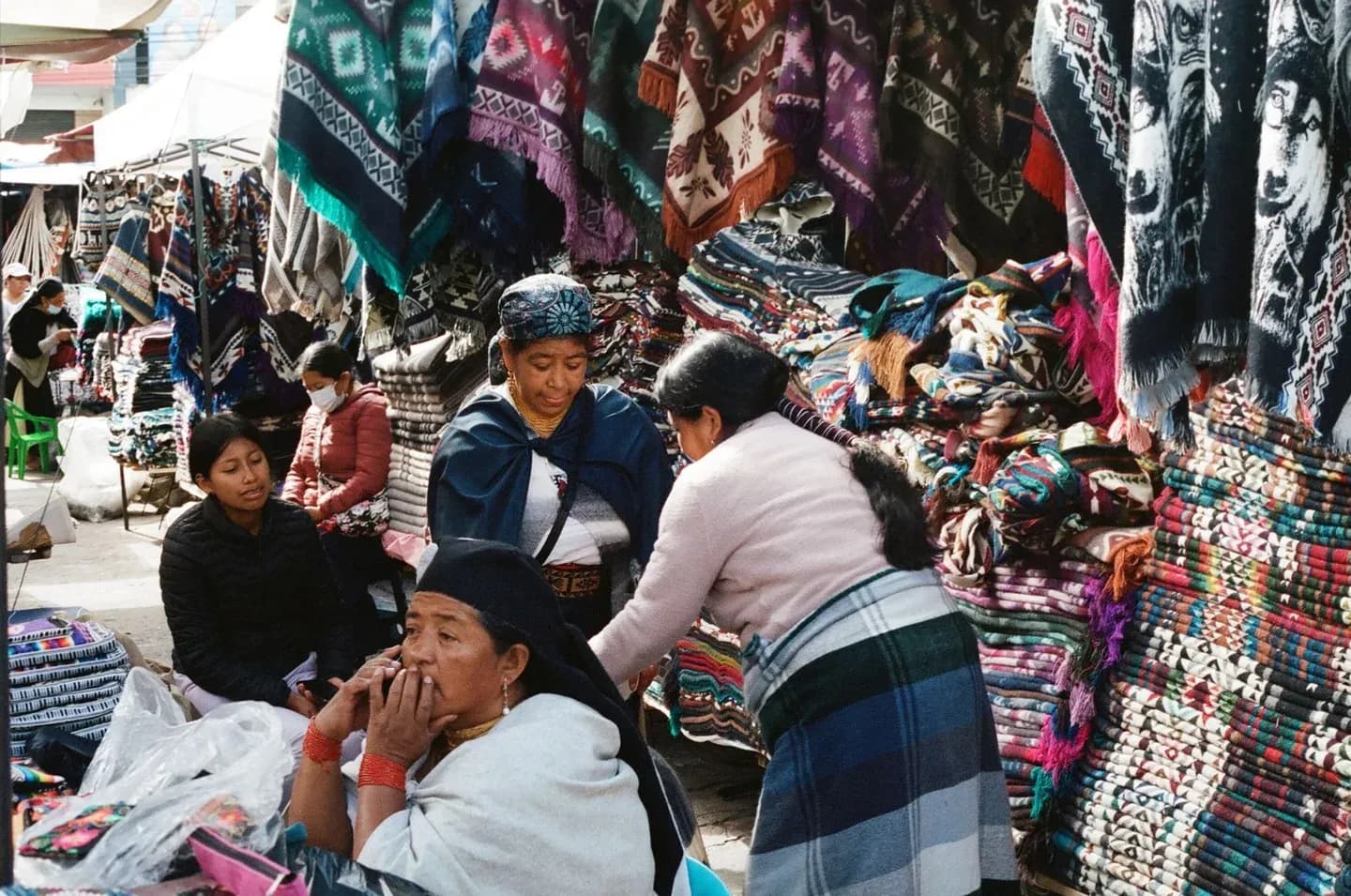 Kichwa women among woven textiles at the Otavalo market, Ecuador