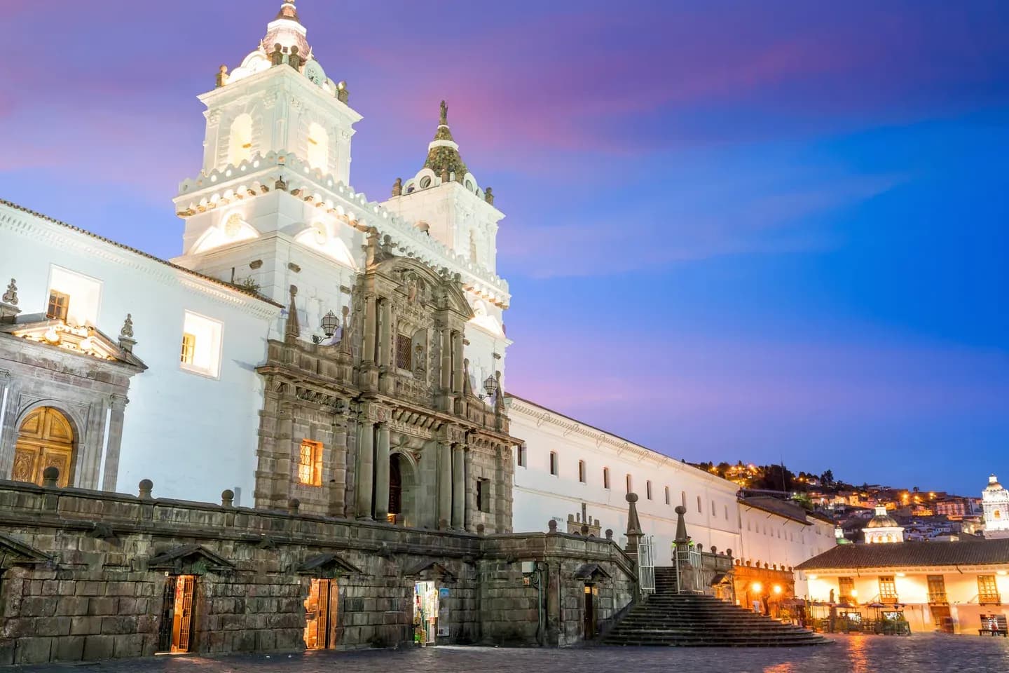 The twin towers of San Francisco church lit at dusk on its plaza in old Quito, Ecuador