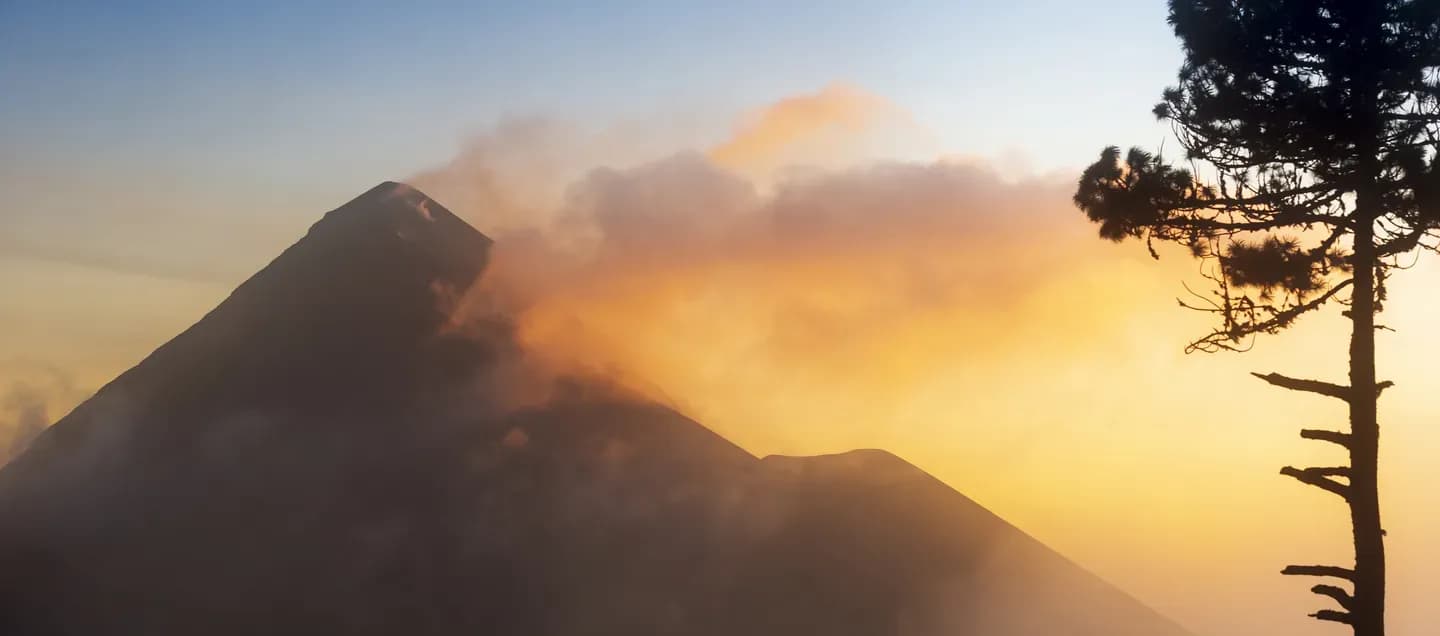 Silhouette of Volcan de Fuego with an ash plume glowing orange at sunset, Guatemala