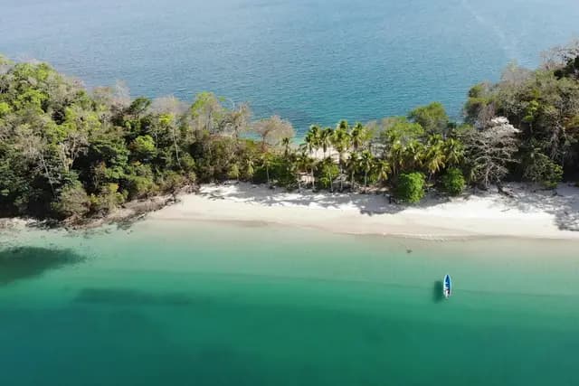 Aerial view of a turquoise cove, white-sand beach and forested island with a small boat, Panama