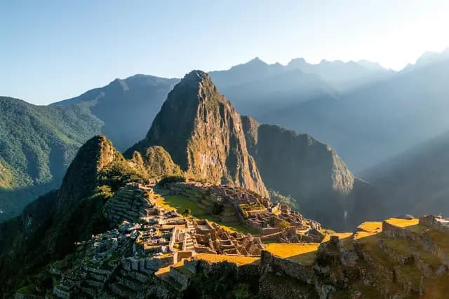 Machu Picchu lit by low golden sunlight, with Huayna Picchu rising behind the Inca terraces, Peru