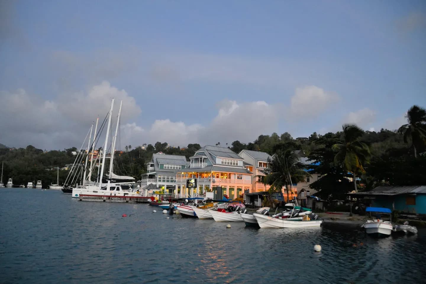 Boats moored at dusk in front of colourful waterfront buildings and palm trees in Marigot Bay, Saint Lucia