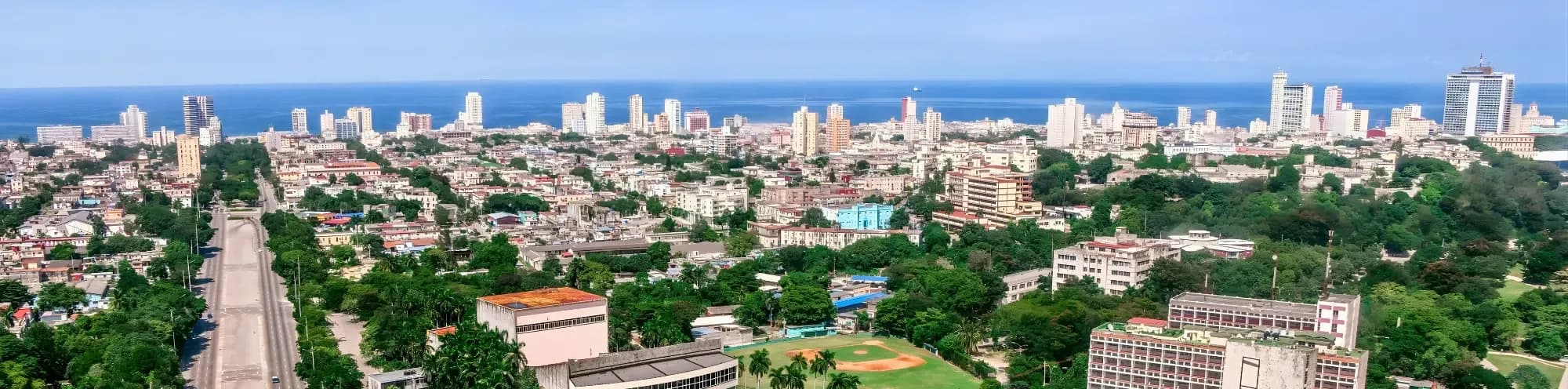 Panoramic view of Havana, Cuba, with the ocean in the background and lush greenery interspersed with buildings.