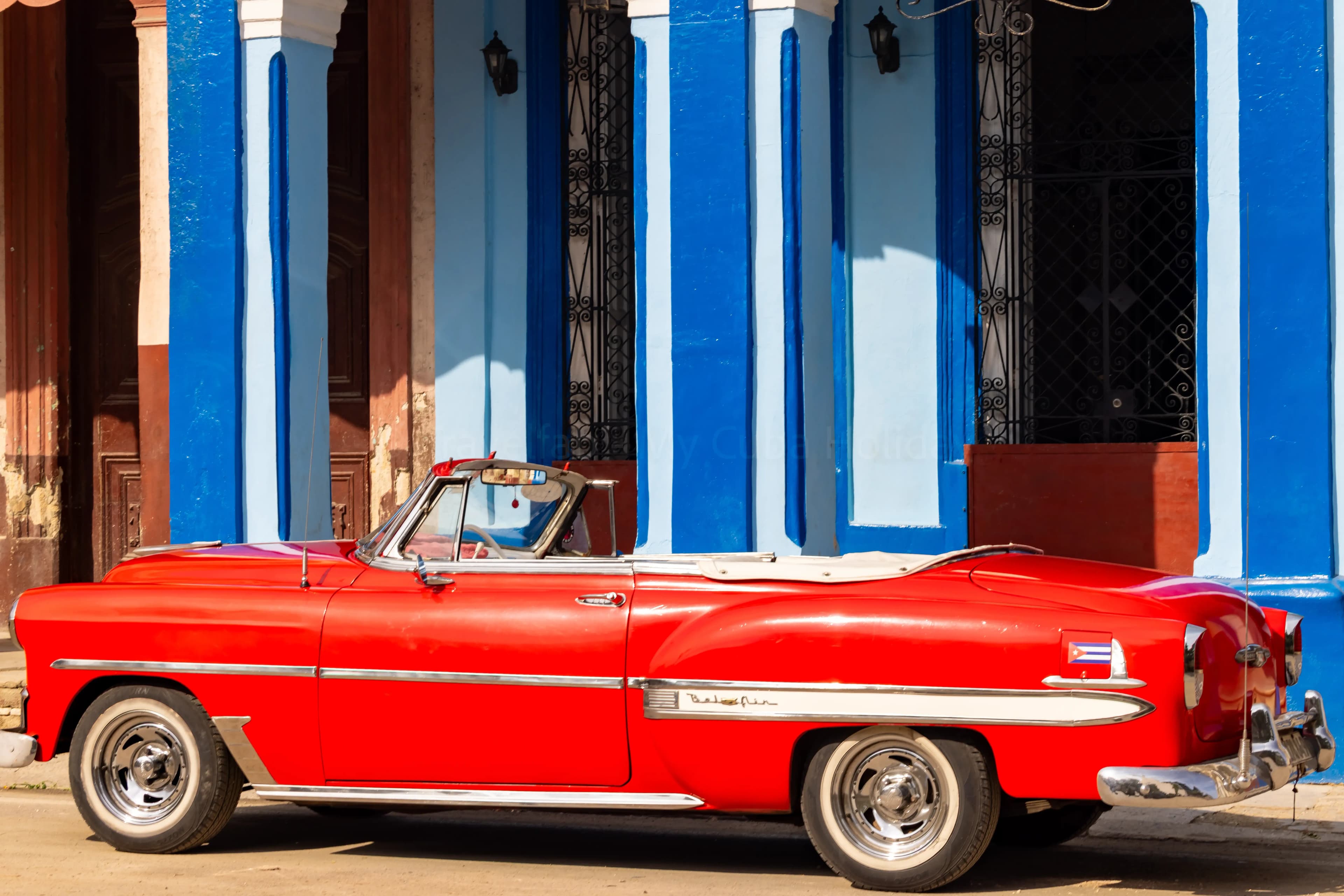 Classic red Chevrolet Bel Air convertible parked outside a blue colonial building in Cuba
