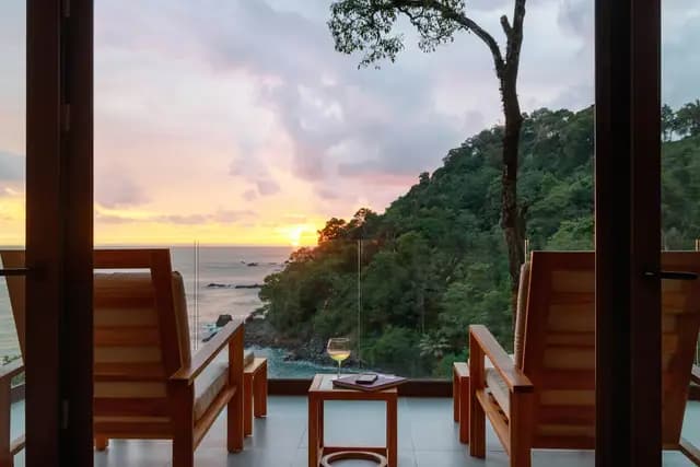 Sunset over the Pacific from the terrace of an Ocean View Premium Suite at Arenas del Mar, Manuel Antonio, two chairs and a glass of wine