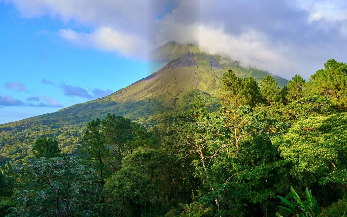 Arenal Volcano with a cloud-wisped summit rising above lush green rainforest in Costa Rica