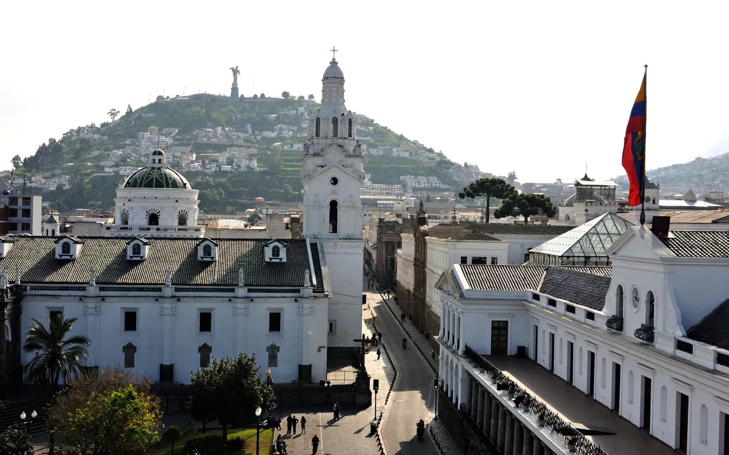 The white Metropolitan Cathedral tower on Plaza Grande in Quito's old town, with El Panecillo and its Virgin on the hill behind