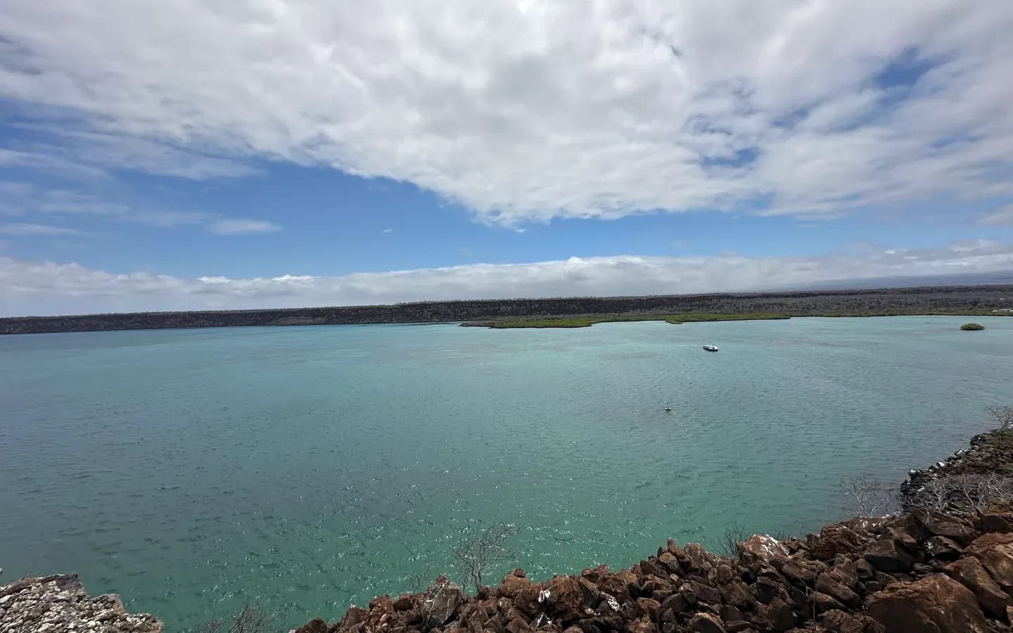 A teal lagoon behind a lava shoreline under a wide cloudy sky on Santa Cruz island, Galápagos