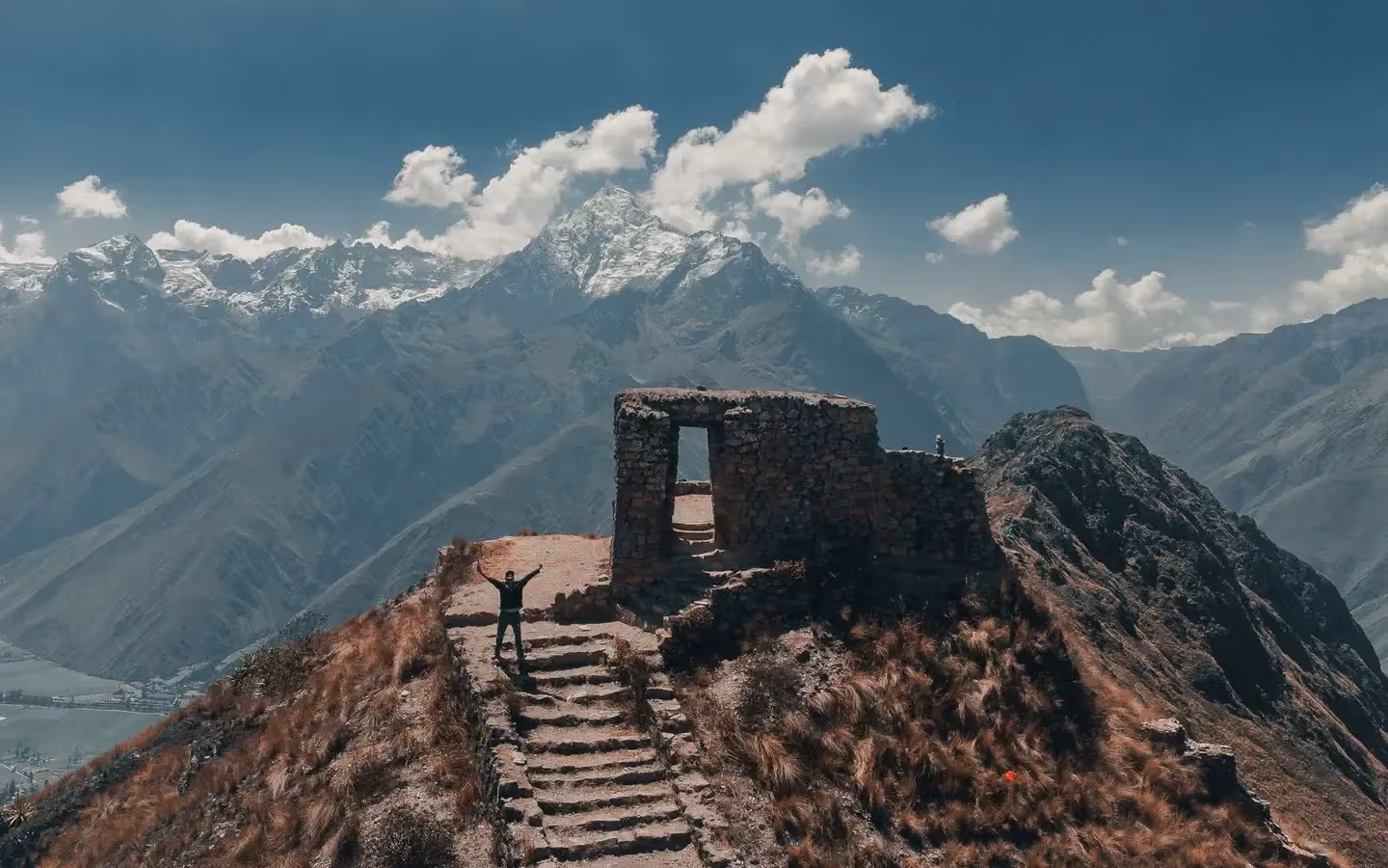 A trekker at a stone Inca gateway on the trail, with snow-capped Andean peaks behind