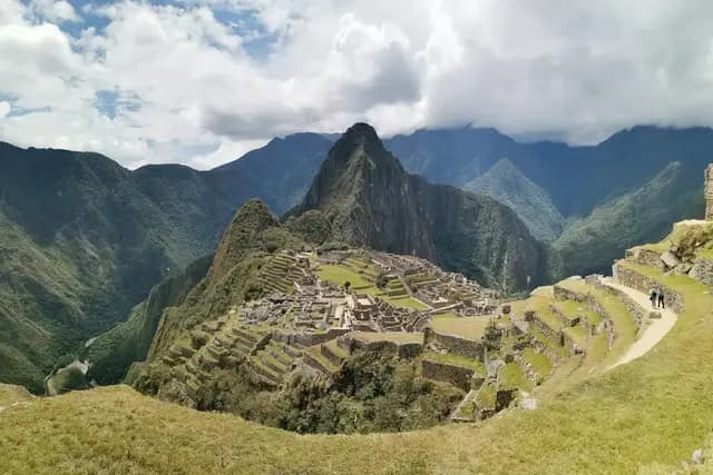 Panoramic view of the ancient Inca citadel of Machu Picchu with Huayna Picchu mountain rising behind, surrounded by lush green Andean peaks