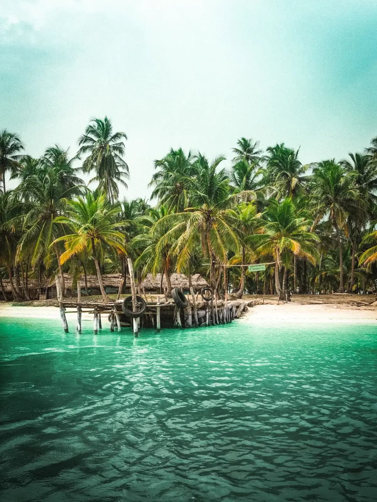 Palm-fringed beach with a wooden stilt dock on a Guna Yala island, San Blas, Panama