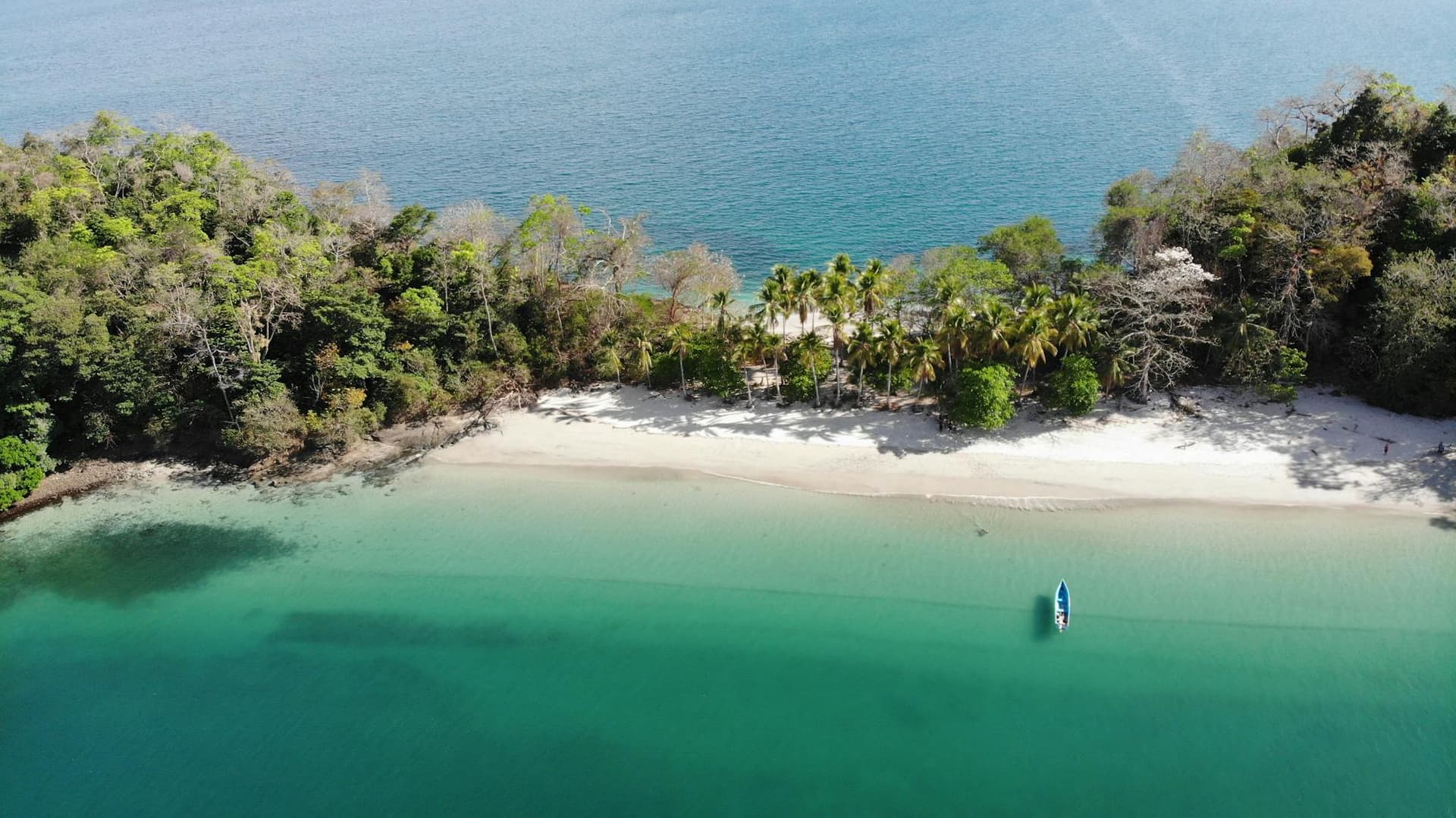 Aerial view of a turquoise cove, white-sand beach and forested island with a small boat, Panama