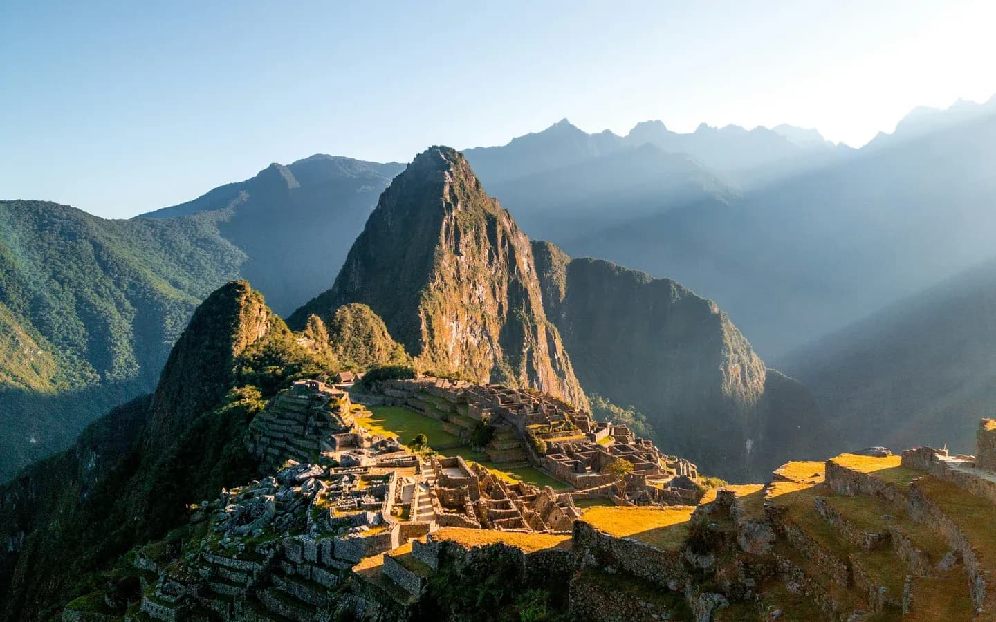 Machu Picchu lit by low golden sunlight, with Huayna Picchu rising behind the Inca terraces, Peru