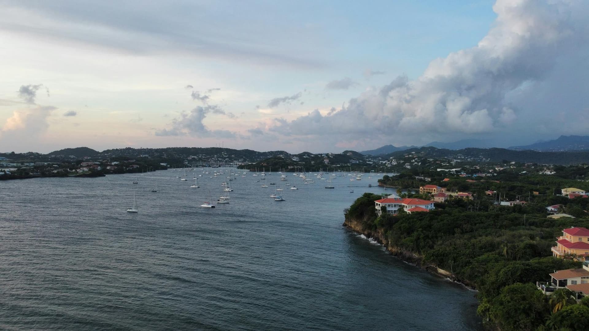 Aerial view of yachts and boats anchored in a sheltered Saint Lucia bay at dusk, with a coastal town beyond